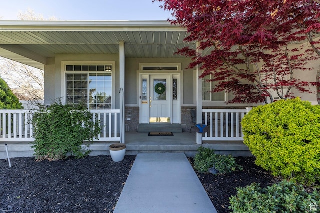 doorway to property featuring stone siding, stucco siding, and covered porch