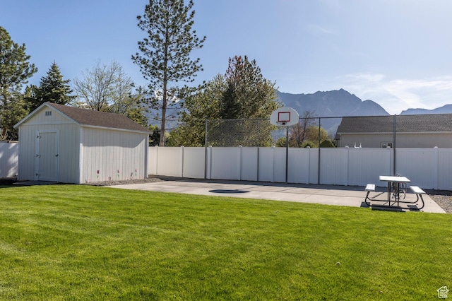 view of yard featuring fence, an outdoor structure, a mountain view, a shed, and basketball court