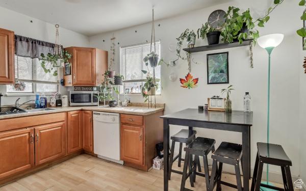 kitchen with brown cabinetry, white dishwasher, a sink, and stainless steel microwave
