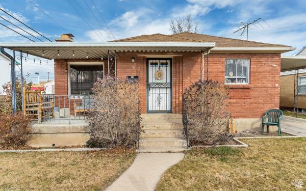 bungalow with a porch, a chimney, brick siding, and a front yard