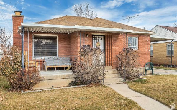 bungalow-style home with a front lawn, a chimney, and covered porch