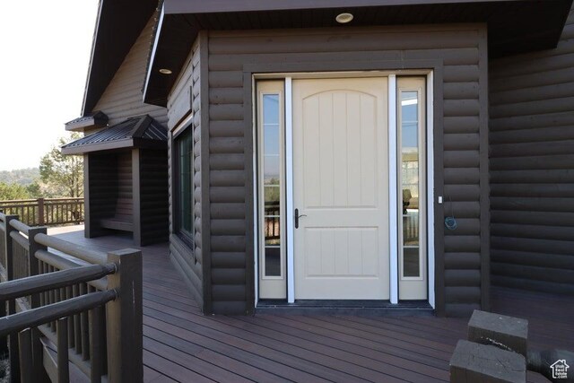 view of exterior entry with a deck and log veneer siding