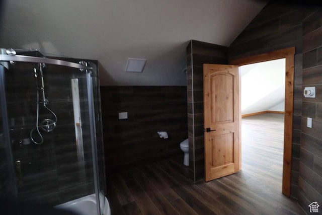 bathroom featuring toilet, wood finished floors, a stall shower, wood walls, and lofted ceiling