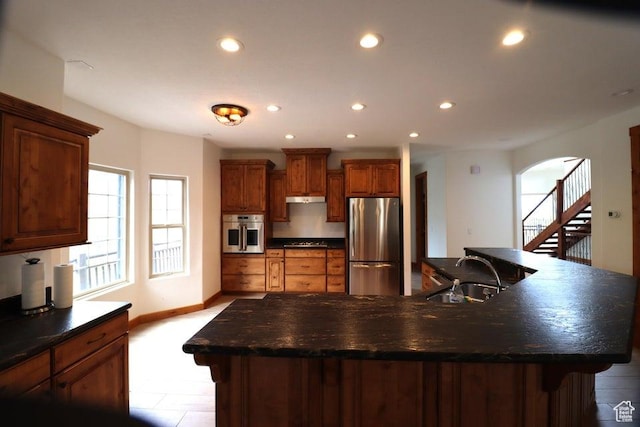 kitchen with a sink, stainless steel appliances, under cabinet range hood, and dark countertops