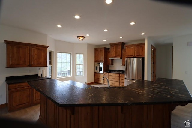 kitchen featuring freestanding refrigerator, recessed lighting, under cabinet range hood, a breakfast bar, and a sink