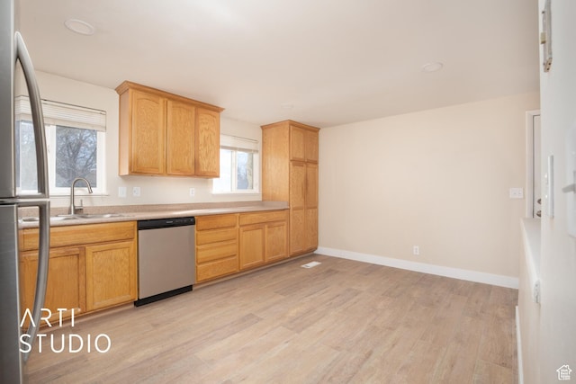 kitchen featuring a sink, stainless steel appliances, light wood-type flooring, light countertops, and baseboards