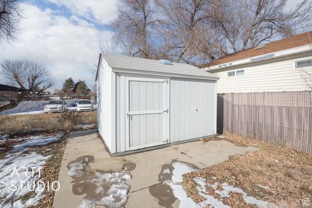 snow covered structure featuring a fenced backyard, a storage unit, and an outbuilding