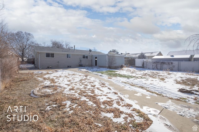 snow covered back of property with fence and brick siding