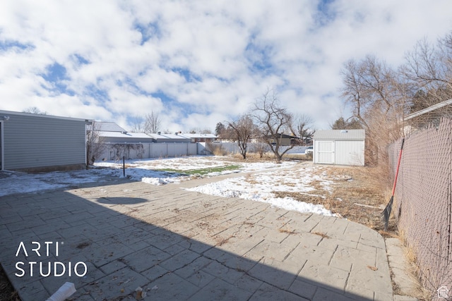 yard layered in snow with a patio, an outdoor structure, fence, and a shed