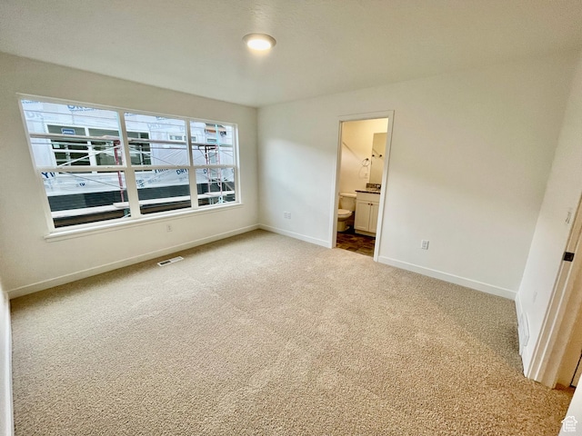unfurnished bedroom featuring ensuite bath, carpet flooring, baseboards, and visible vents