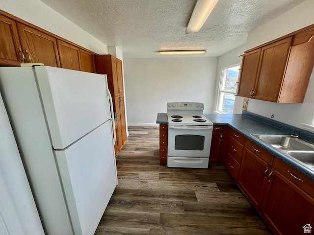kitchen with a sink, white appliances, a textured ceiling, dark wood-style floors, and dark countertops