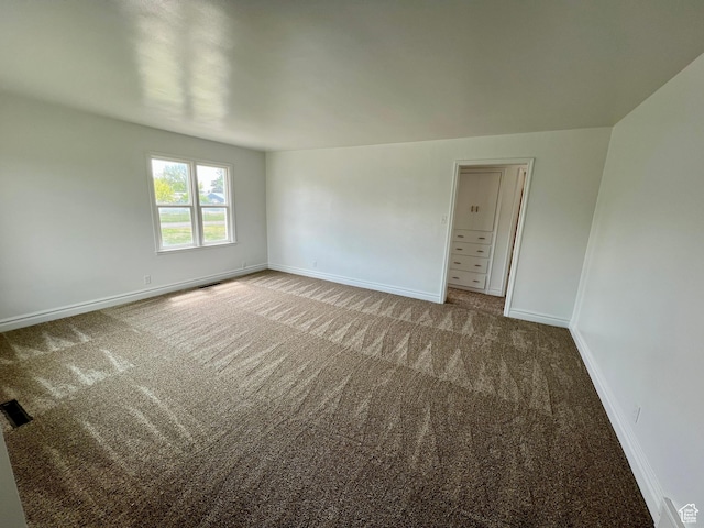 empty room with carpet flooring, visible vents, and baseboards