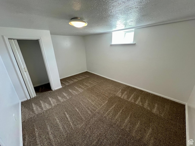 basement featuring a textured ceiling, baseboards, and dark carpet