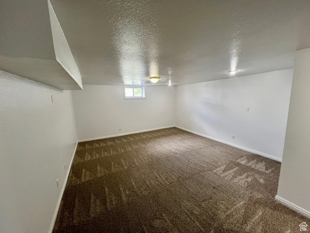 below grade area featuring a textured ceiling, carpet, and baseboards