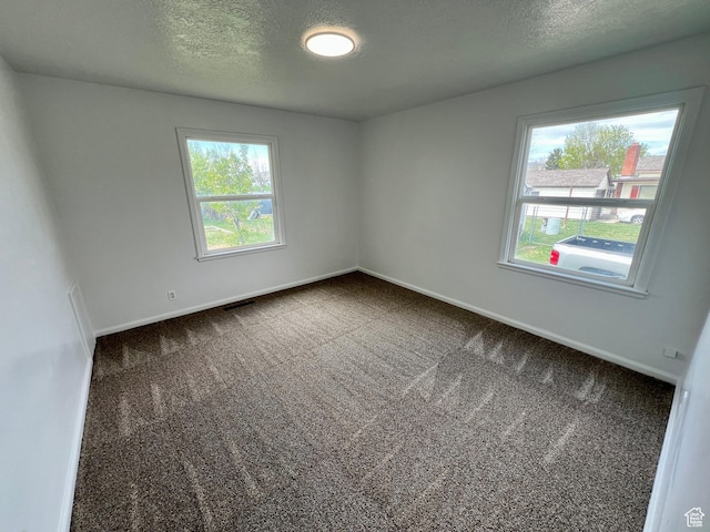 unfurnished room with a healthy amount of sunlight, visible vents, baseboards, and dark carpet