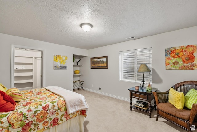 bedroom featuring a walk in closet, a textured ceiling, visible vents, baseboards, and light carpet