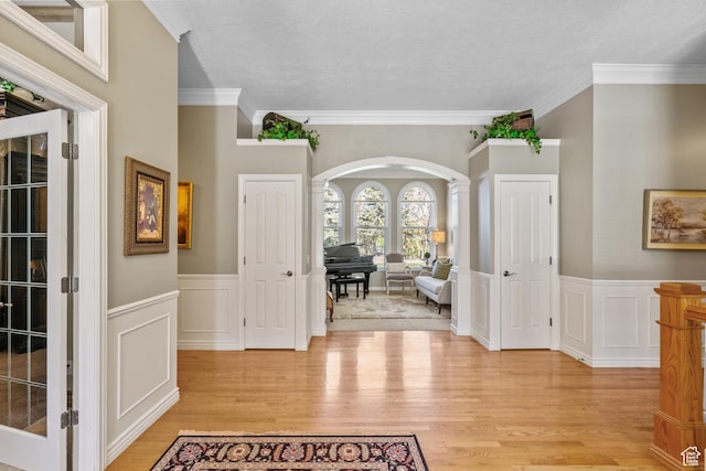 foyer with crown molding, light wood-style flooring, a wainscoted wall, and arched walkways