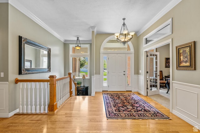 entrance foyer featuring a chandelier, a decorative wall, light wood-style flooring, and a healthy amount of sunlight
