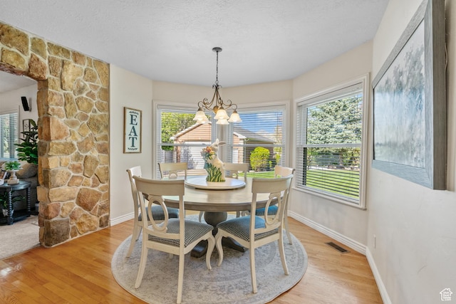 dining space featuring a textured ceiling, baseboards, visible vents, a chandelier, and light wood-style floors