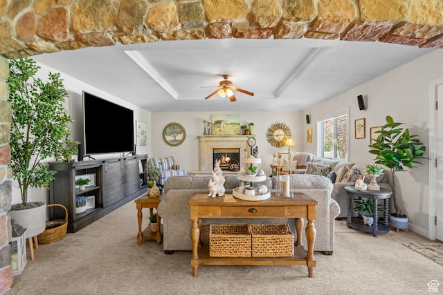 carpeted living area with a tray ceiling, a ceiling fan, and a glass covered fireplace