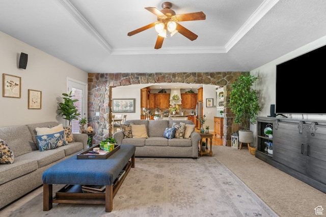 living room with light carpet, a raised ceiling, crown molding, and a ceiling fan