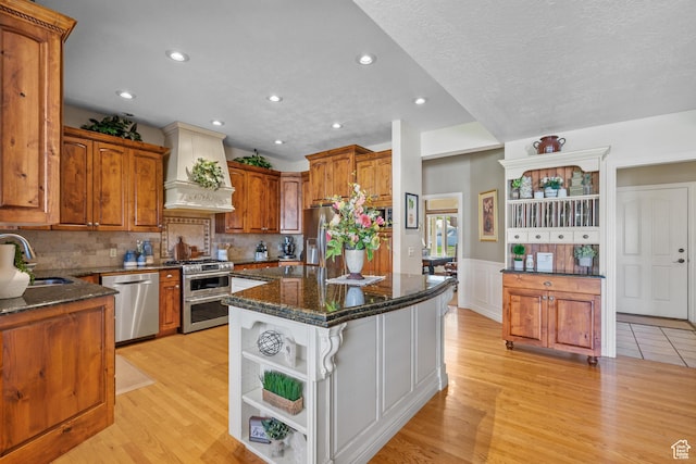 kitchen with a sink, stainless steel appliances, open shelves, custom exhaust hood, and light wood finished floors