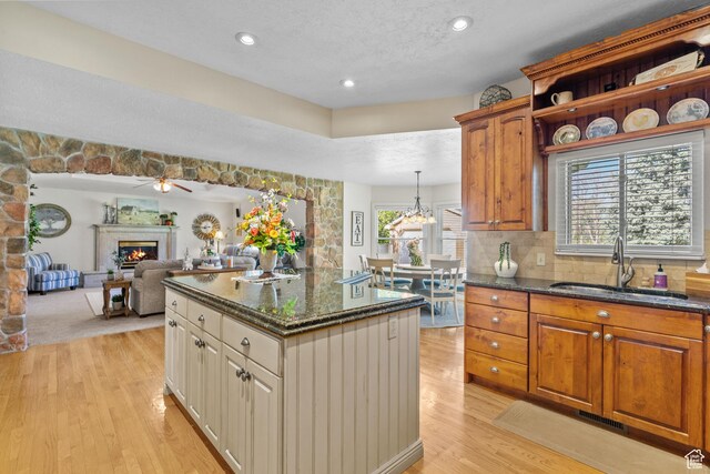 kitchen featuring a sink, dark stone counters, light wood finished floors, a center island, and a glass covered fireplace