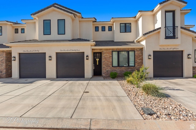 multi unit property with stucco siding, driveway, brick siding, and a garage