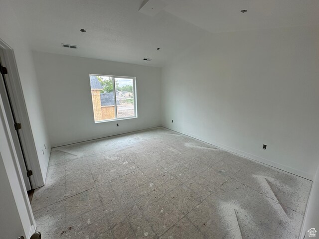 empty room featuring vaulted ceiling, visible vents, and baseboards