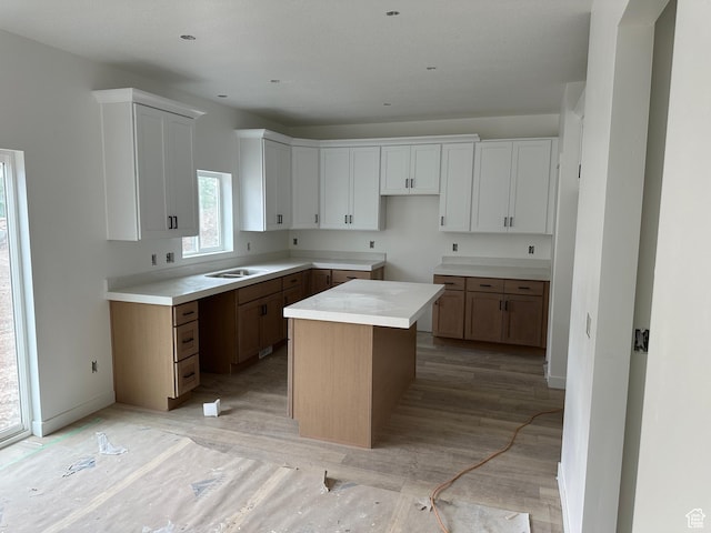 kitchen with light wood finished floors, white cabinets, a sink, and a kitchen island