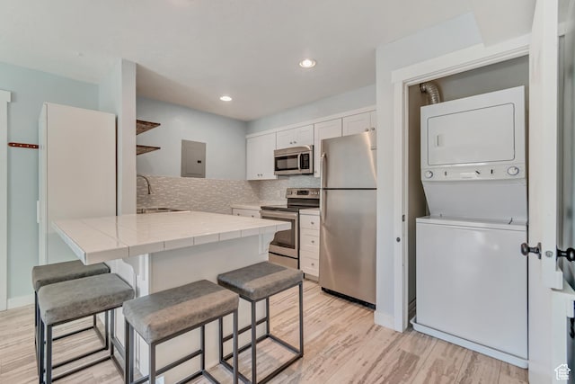 kitchen with a sink, stacked washing maching and dryer, open shelves, tile counters, and appliances with stainless steel finishes