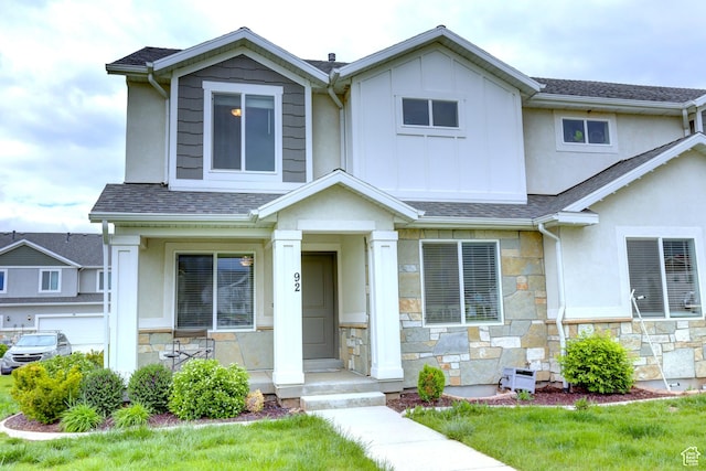 view of front facade with a shingled roof, stucco siding, stone siding, and board and batten siding
