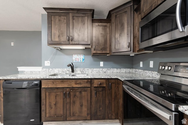 kitchen featuring a sink, a textured ceiling, light stone countertops, dark brown cabinets, and appliances with stainless steel finishes