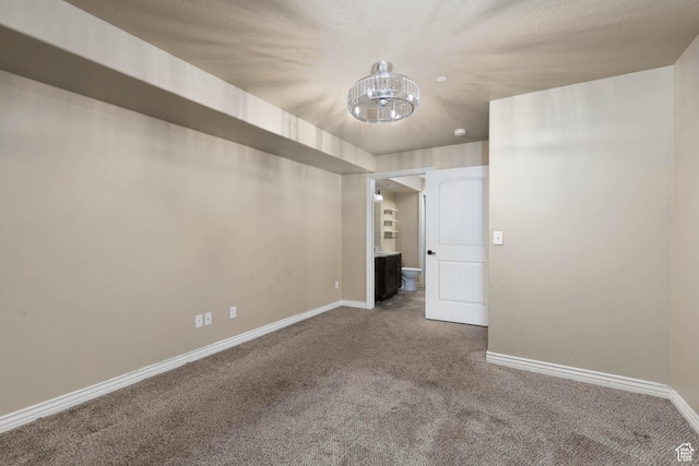 empty room featuring a chandelier, carpet floors, and baseboards