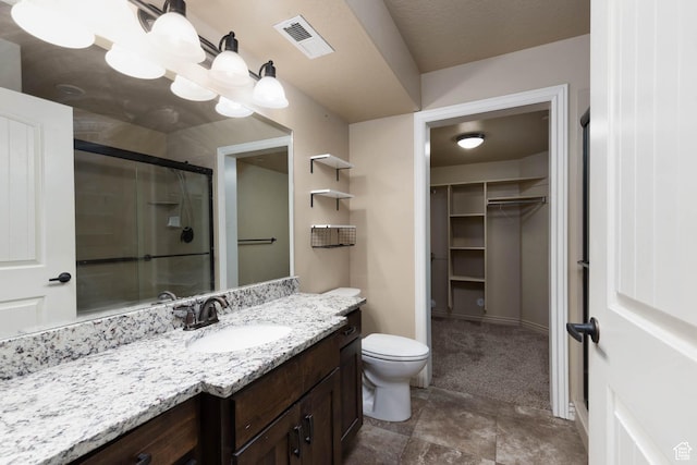 bathroom featuring toilet, a stall shower, a walk in closet, visible vents, and vanity