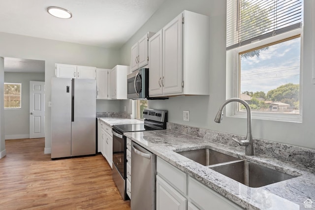 kitchen featuring light stone countertops, light wood-style flooring, a sink, stainless steel appliances, and white cabinets