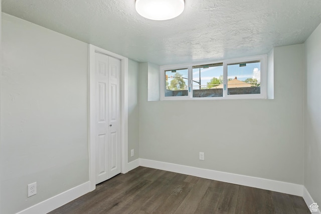 empty room featuring dark wood-style flooring, a textured ceiling, and baseboards