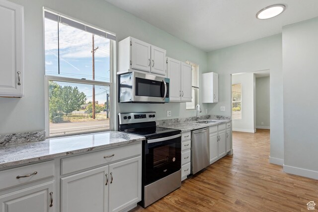 kitchen featuring a sink, appliances with stainless steel finishes, white cabinets, light stone countertops, and light wood-style floors