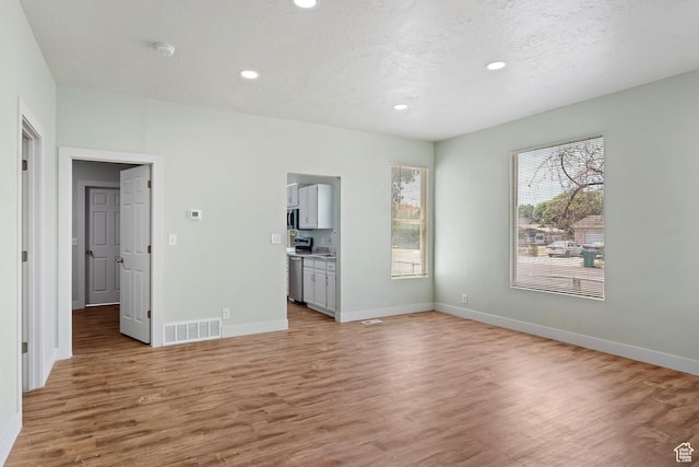 unfurnished living room featuring light wood-type flooring, visible vents, baseboards, and recessed lighting
