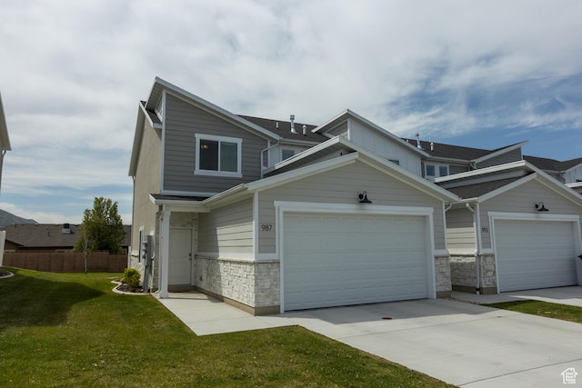 multi unit property with stone siding, driveway, a front lawn, and fence