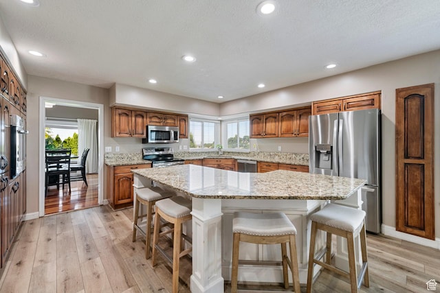 2247 Country Oaks Dr, Layton, UT 84040 - kitchen with stainless steel appliances, brown cabinetry, light wood finished floors, a breakfast bar, and a center island