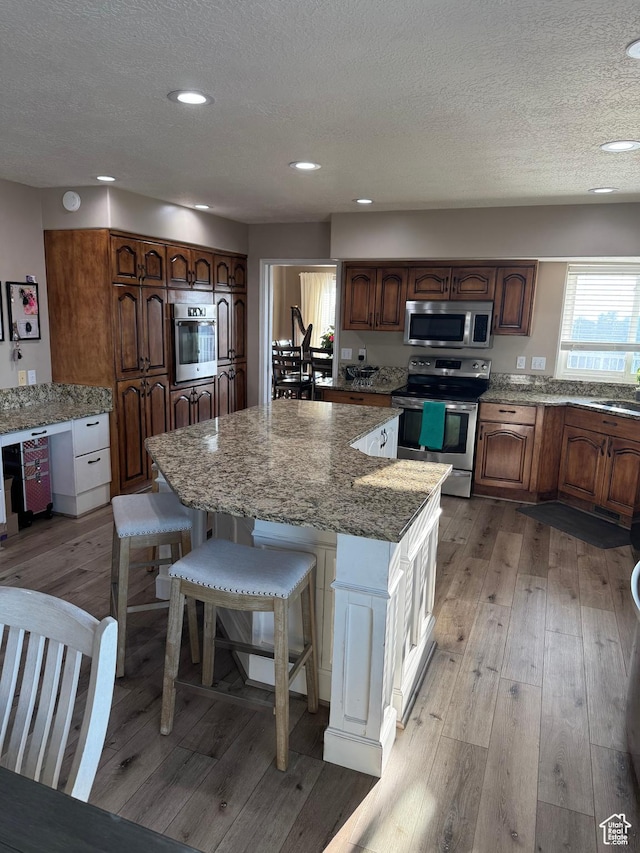 2247 Country Oaks Dr, Layton, UT 84040 - kitchen with a center island, light wood-style flooring, a sink, stainless steel appliances, and a textured ceiling