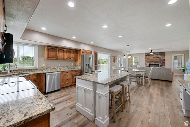 2247 Country Oaks Dr, Layton, UT 84040 - kitchen with appliances with stainless steel finishes, brown cabinetry, plenty of natural light, a stone fireplace, and a textured ceiling