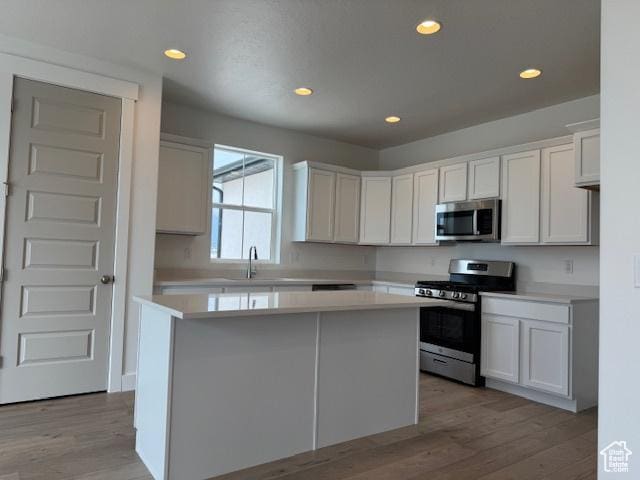 kitchen with light wood finished floors, a center island, stainless steel appliances, white cabinets, and light countertops