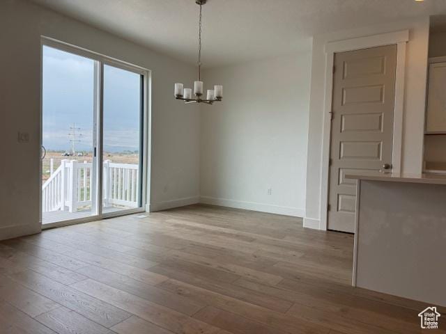 unfurnished dining area featuring plenty of natural light, hardwood / wood-style flooring, baseboards, and a notable chandelier