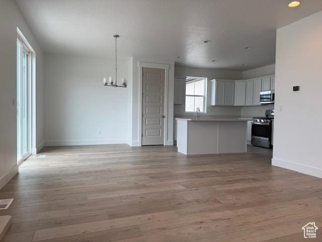 unfurnished living room with light wood finished floors, a sink, baseboards, a chandelier, and recessed lighting