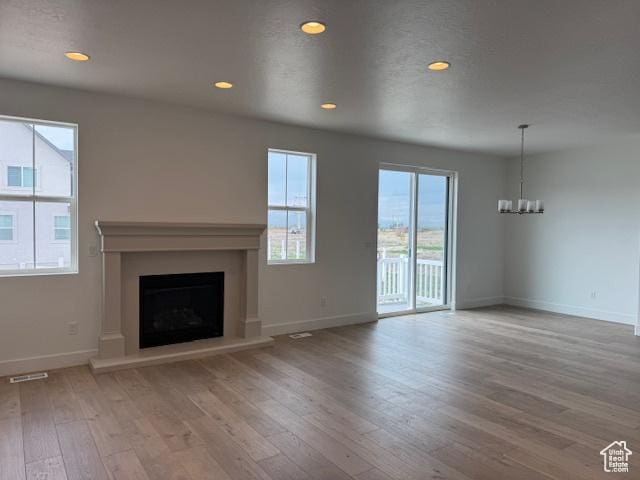 unfurnished living room featuring a notable chandelier, recessed lighting, a fireplace with raised hearth, baseboards, and hardwood / wood-style flooring