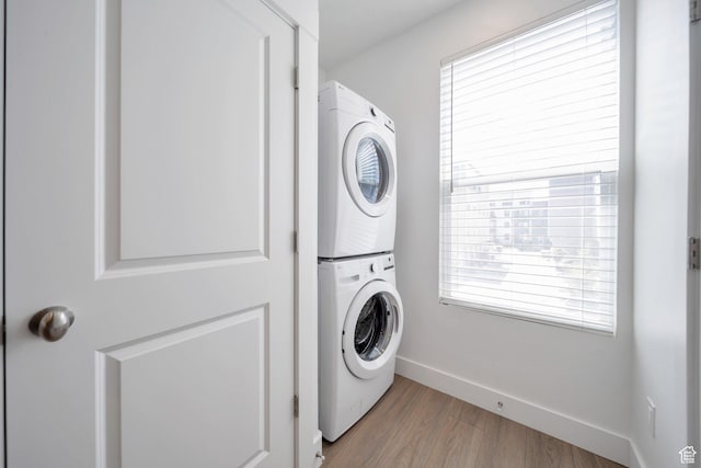 clothes washing area featuring baseboards, a healthy amount of sunlight, stacked washer / dryer, and wood finished floors