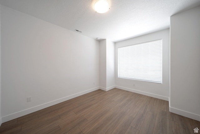 unfurnished room featuring a textured ceiling, baseboards, visible vents, and wood finished floors