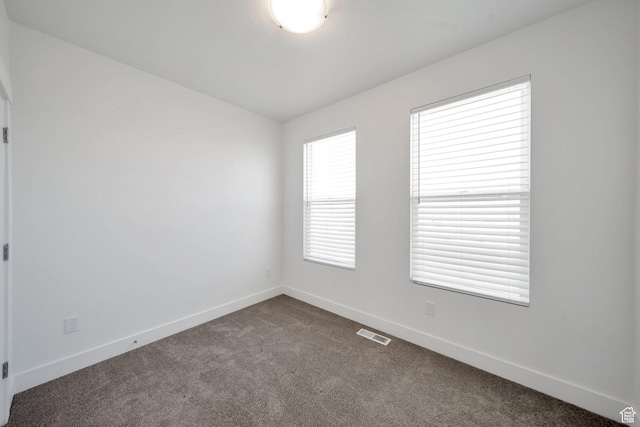 unfurnished room with baseboards, visible vents, and dark carpet